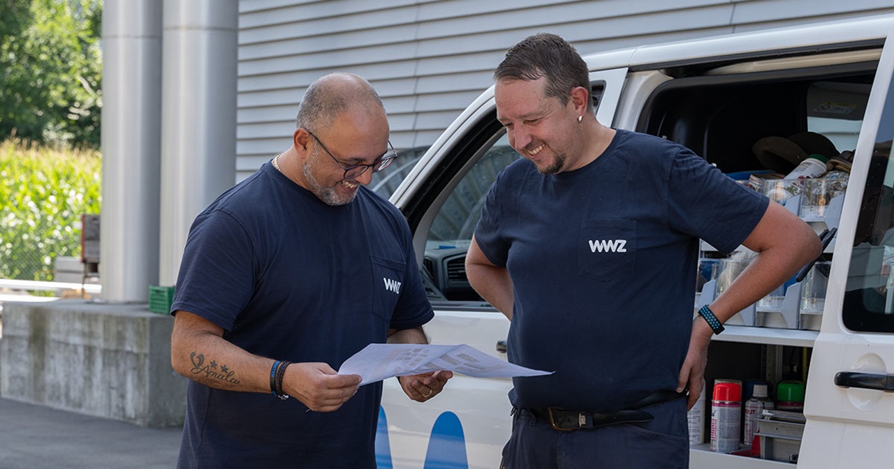 Zwei Männer stehen vor WWZ-Auto und schauen sich einen Plan an.